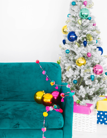 teal couch with a strand of ornaments on it and a white christmas tree with big and small ornaments.